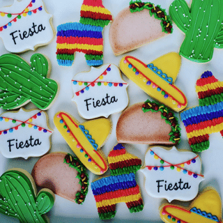 Colorful fiesta-themed cookies shaped like cacti, tacos, sombreros, a piñata, and signs reading Fiesta, decorated with bright icing and festive designs.